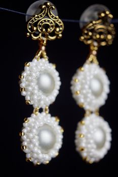 handmade jewelry made of beads in macro. earrings from white beads. earrings from stones. beautiful ornaments. earrings from white beads. ornaments on a black background