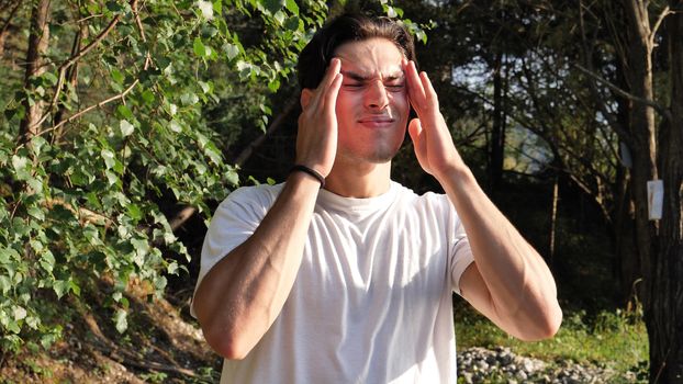 Young handsome man standing in nature, in pain, suffering from headache or migraine