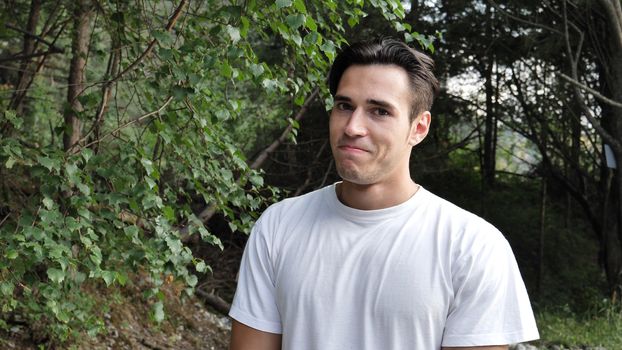 Young handsome man standing in nature, trying not to laugh then bursting into laughter