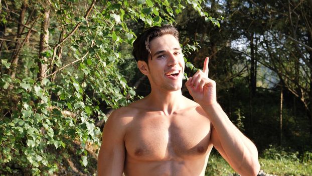 Young handsome shirtless muscular man having an idea while thinking, standing in nature
