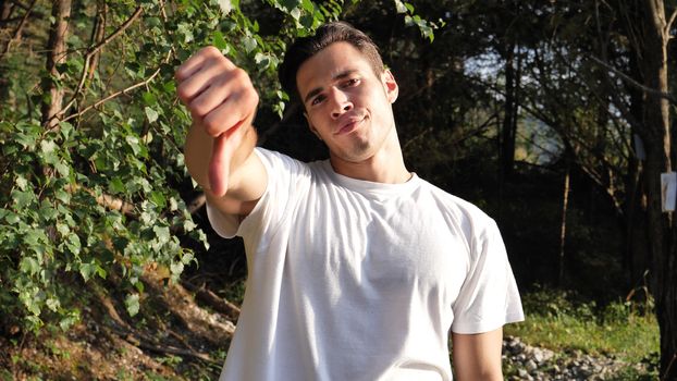 Young handsome man standing in nature, unhappy or displeased, doing thumb down sign