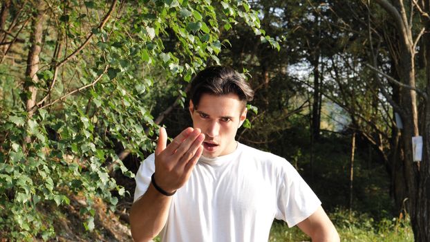 Young handsome man standing in nature, saying Come Here or Come Closer with hand gesturing