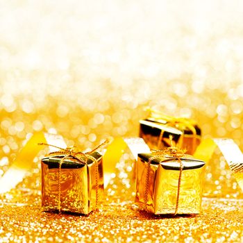 Decorative golden boxes with holiday gifts on shiny glitter background