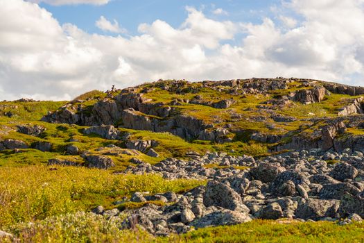 A rocky hill with grass and moss. Over the hill, white clouds play catch-up, creating unimaginable figures. Primordial natural power lies in the Northern landscapes.