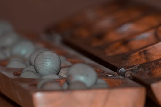 Closeup of a wooden mancala game with grey stones