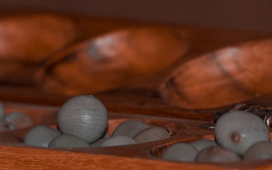 Closeup of a wooden mancala game with grey stones