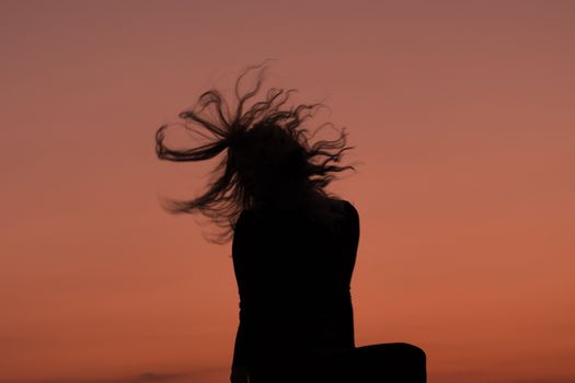 A young female silhouette hair spiral during an orange sunset