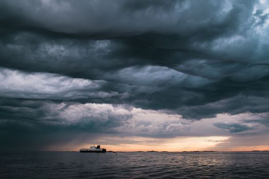 A cargo ship underneath stormy clouds during sunset