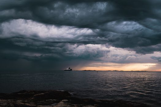 A cargo ship underneath stormy clouds during sunset