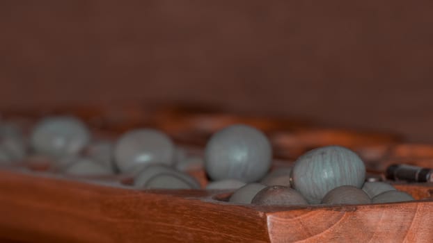 Closeup of a wooden mancala game with grey stones