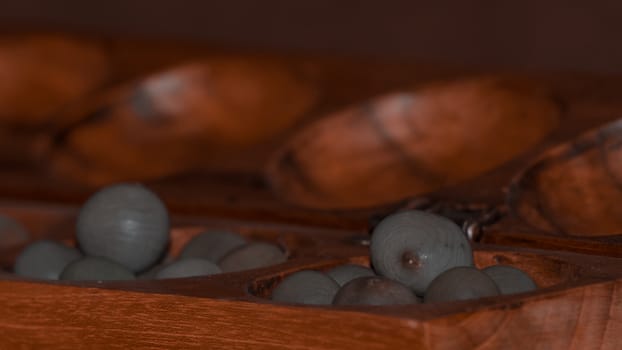 Closeup of a wooden mancala game with grey stones