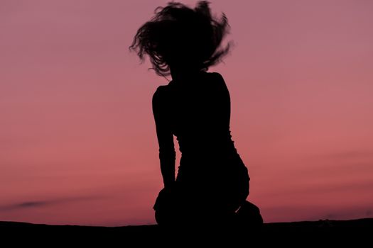 A young female silhouette hair spiral during a pink sunset