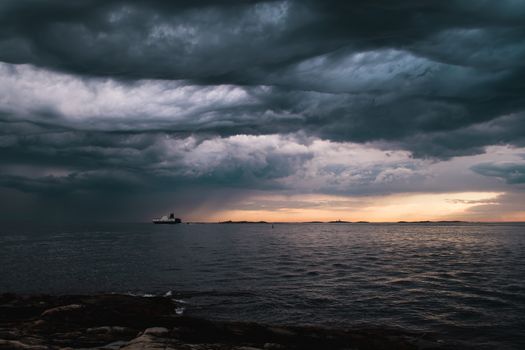 A cargo ship underneath stormy clouds during sunset