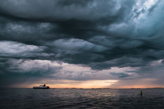 A cargo ship underneath stormy clouds during sunset