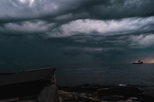 A cargo ship underneath stormy clouds during sunset