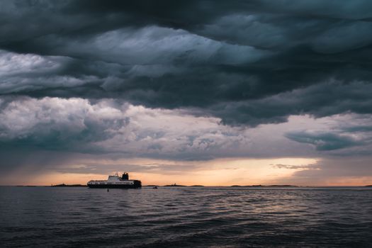 A cargo ship underneath stormy clouds during sunset