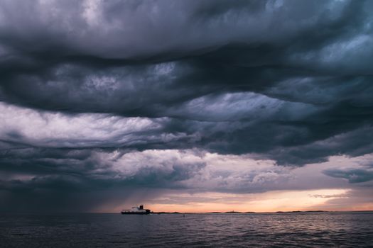 A cargo ship underneath stormy clouds during sunset