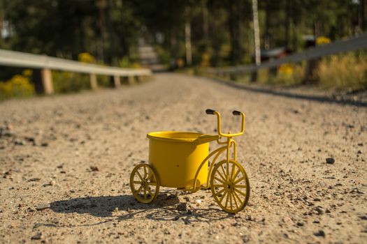 A yellow toy tricycle on a gravel road