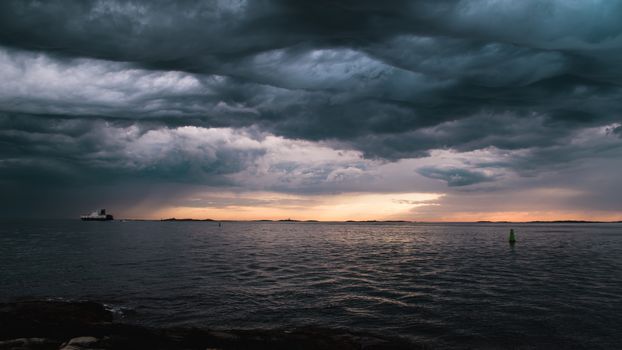 A cargo ship underneath stormy clouds during sunset