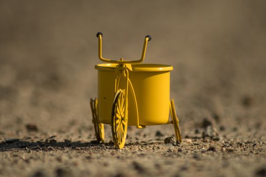 A yellow toy tricycle on a gravel road