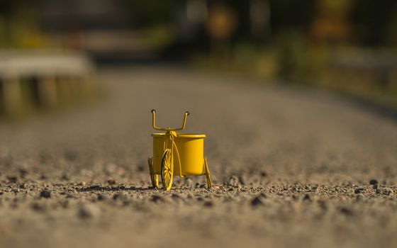 A yellow toy tricycle on a gravel road