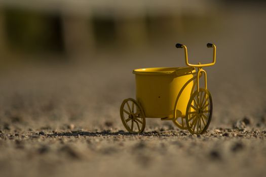 A yellow toy tricycle on a gravel road