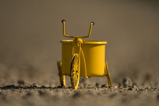 A yellow toy tricycle on a gravel road