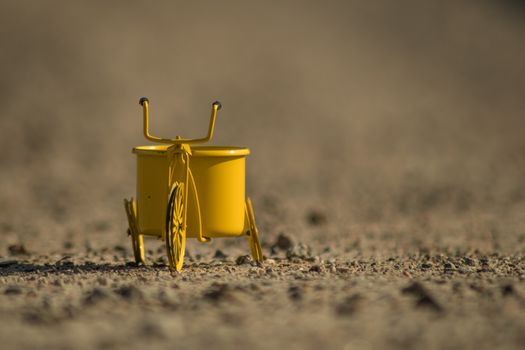 A yellow toy tricycle on a gravel road