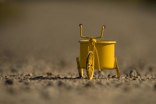 A yellow toy tricycle on a gravel road