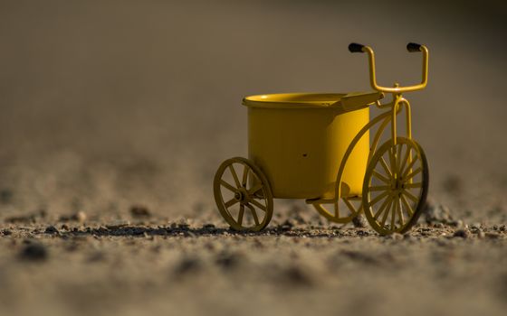 A yellow toy tricycle on a gravel road