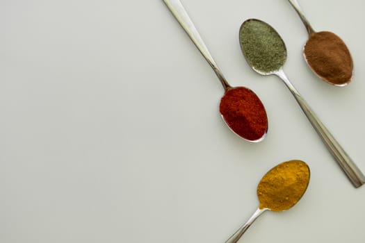 Various colorful spices arranged on spoons  with a white background