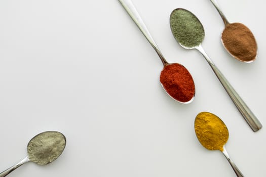 Various colorful spices arranged on spoons  with a white background