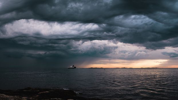 A cargo ship underneath stormy clouds during sunset