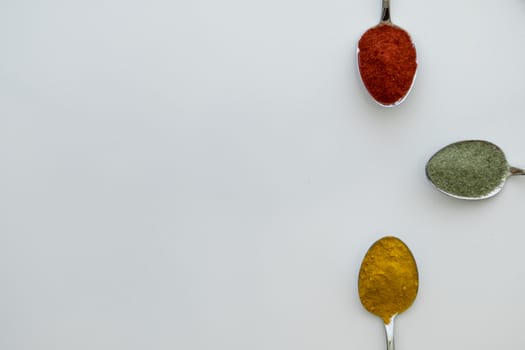 Various colorful spices arranged on spoons  with a white background