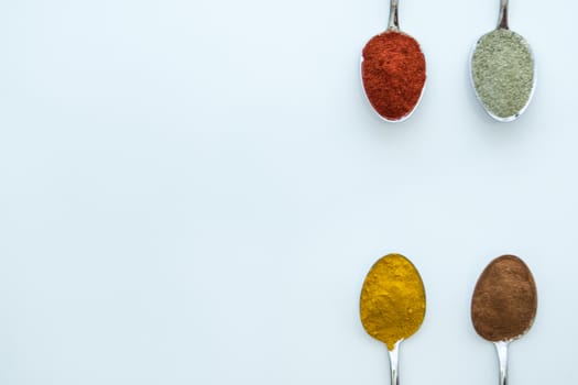 Various colorful spices arranged on spoons  with a white background