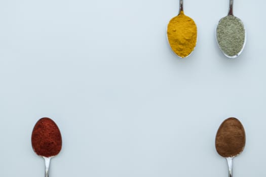 Various colorful spices arranged on spoons  with a white background