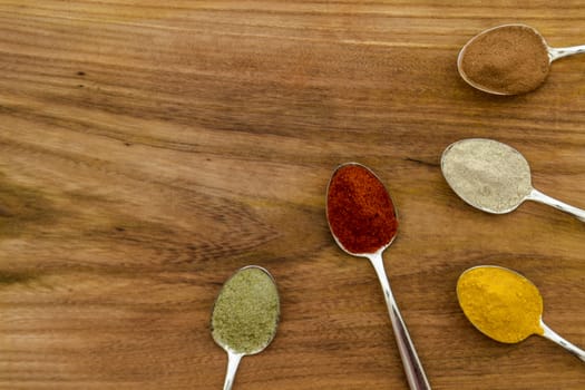 Various colorful spices arranged on spoons  with wooden background