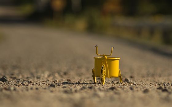 A yellow toy tricycle on a gravel road