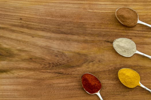 Various colorful spices arranged on spoons  with wooden background