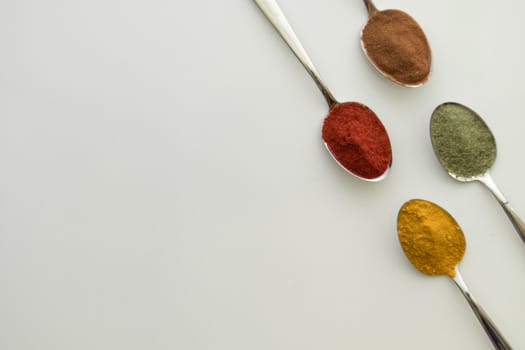 Various colorful spices arranged on spoons  with a white background