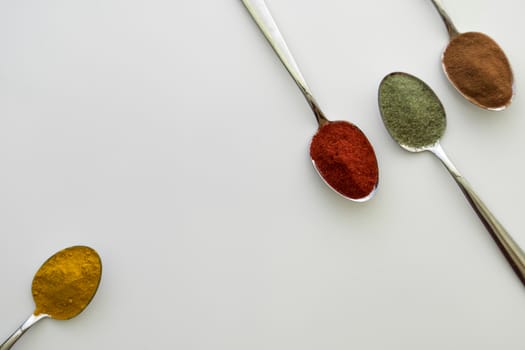 Various colorful spices arranged on spoons  with a white background