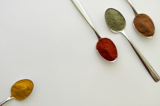 Various colorful spices arranged on spoons  with a white background