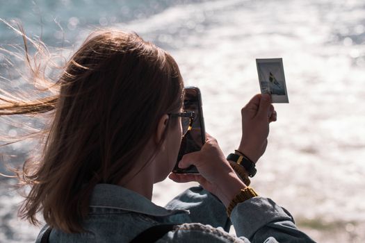 A young girl photographing a polaroid photo with her phone