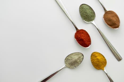 Various colorful spices arranged on spoons  with a white background