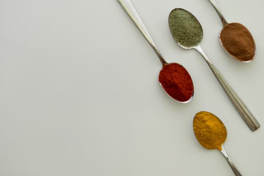 Various colorful spices arranged on spoons  with a white background