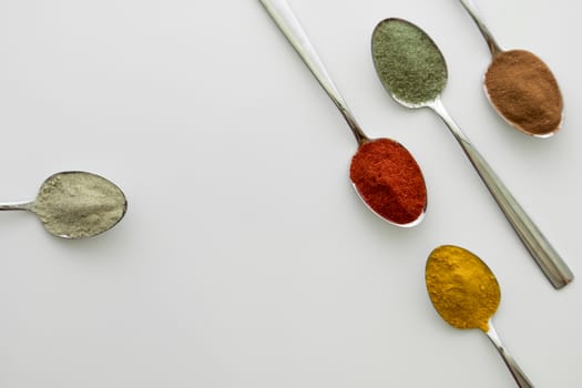 Various colorful spices arranged on spoons  with a white background