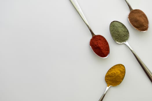 Various colorful spices arranged on spoons  with a white background