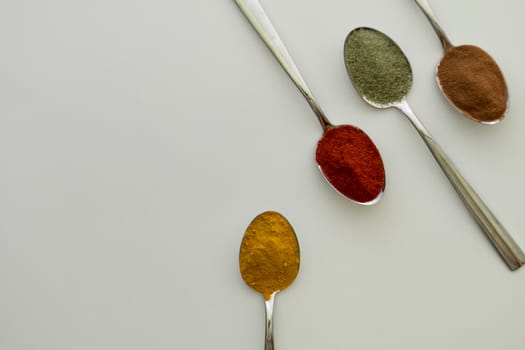 Various colorful spices arranged on spoons  with a white background