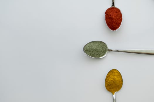 Various colorful spices arranged on spoons  with a white background