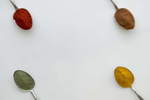 Various colorful spices arranged on spoons  with a white background